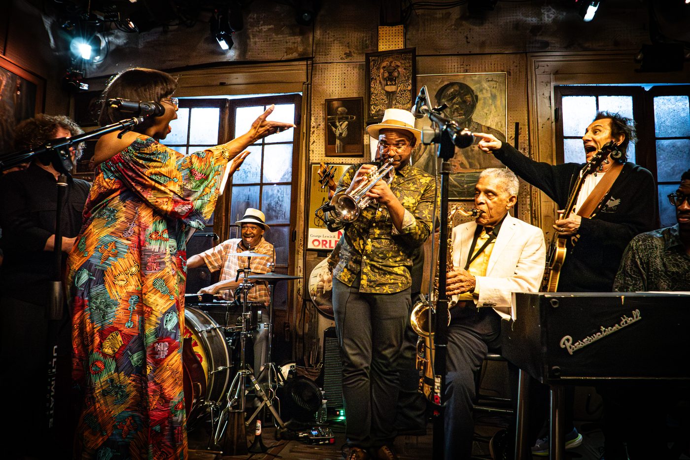 Branden Lewis playing trumpet on the bandstand at Preservation Hall, beside Charlie Gabriel on saxophone, with a singer and full band around them.